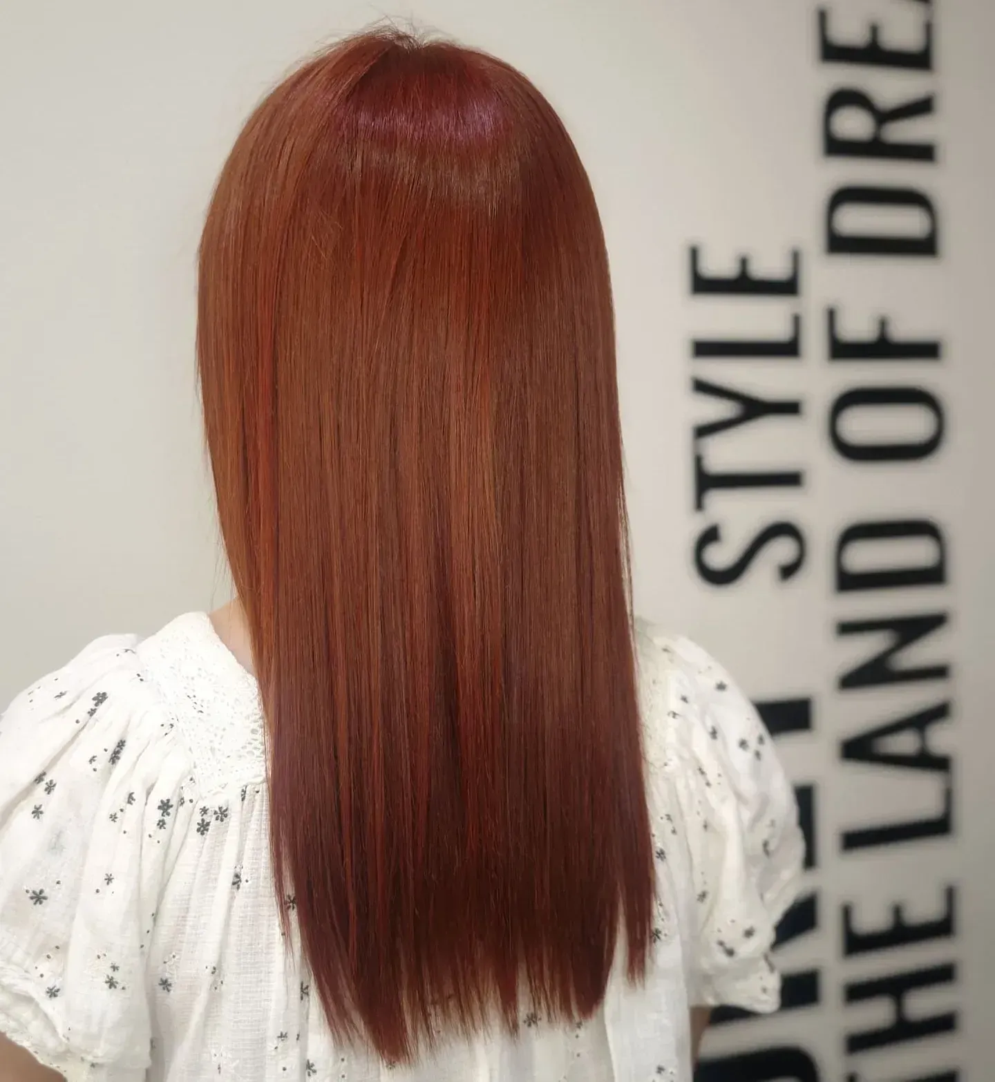 Una mujer con cabello largo y rojo está parada frente a un cartel que dice