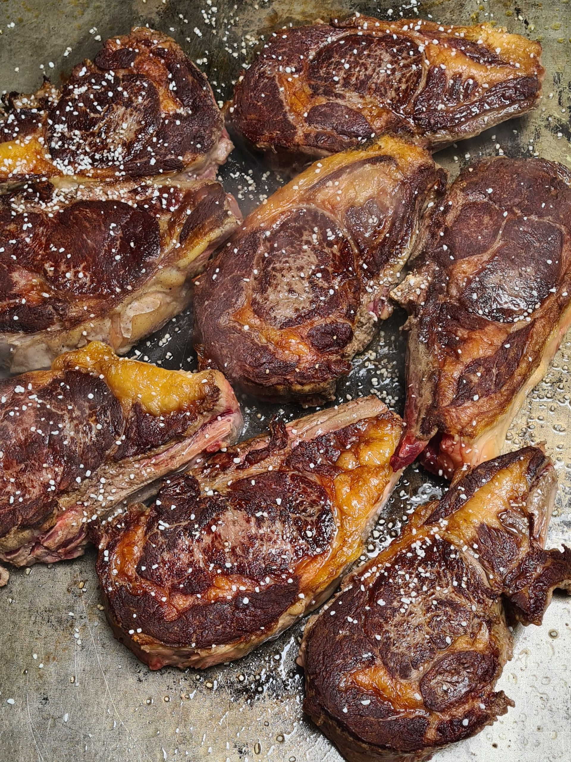 Entrecôtes saisies, avec du gras visible, saupoudrées de gros sel, dans une poêle en métal.