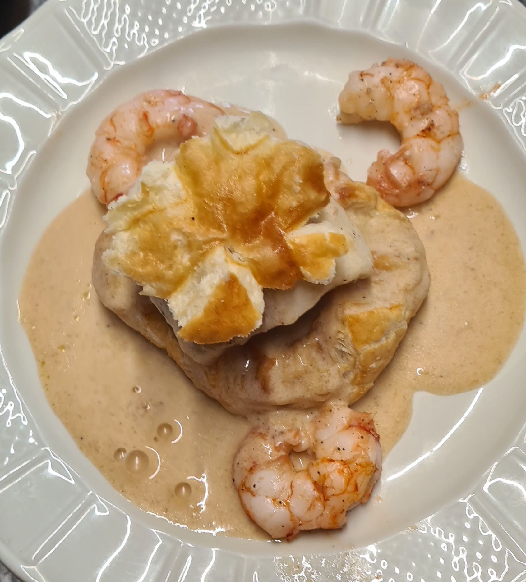 Assiette de poisson en croûte avec sauce crémeuse et trois crevettes.