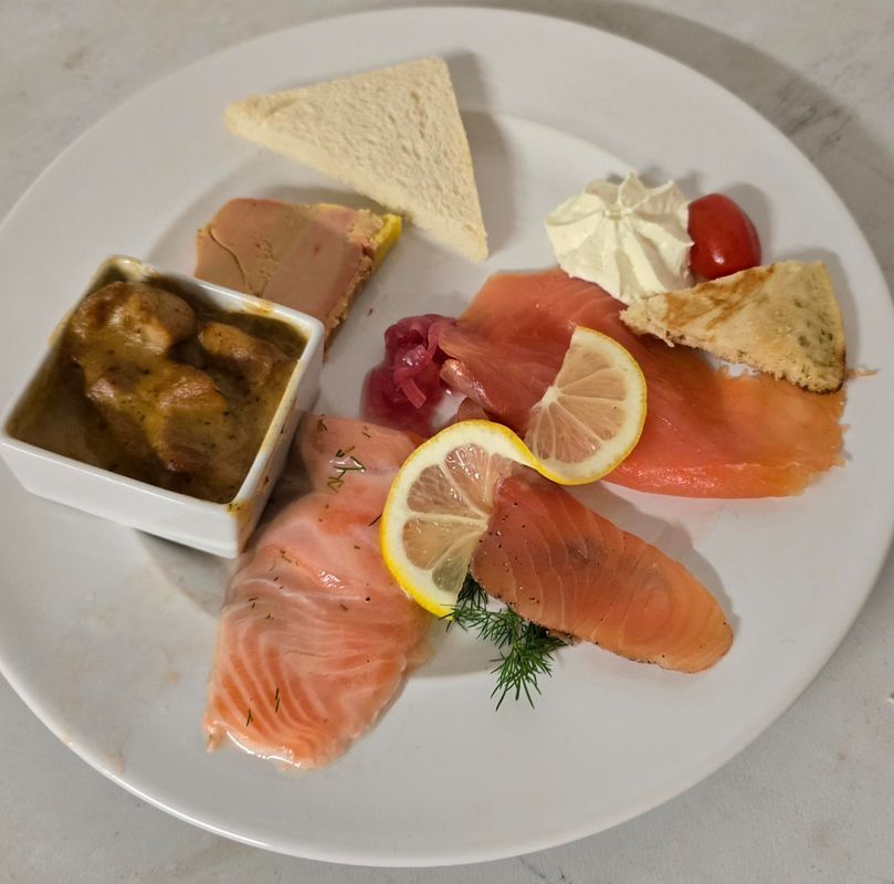 Assiette avec les tranches de saumon fumé, le citron, le foie gras et autres accompagnements.