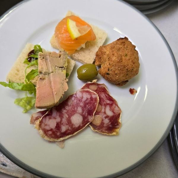 Une assiette avec le foie gras, saucisson, acra et une tartine. 