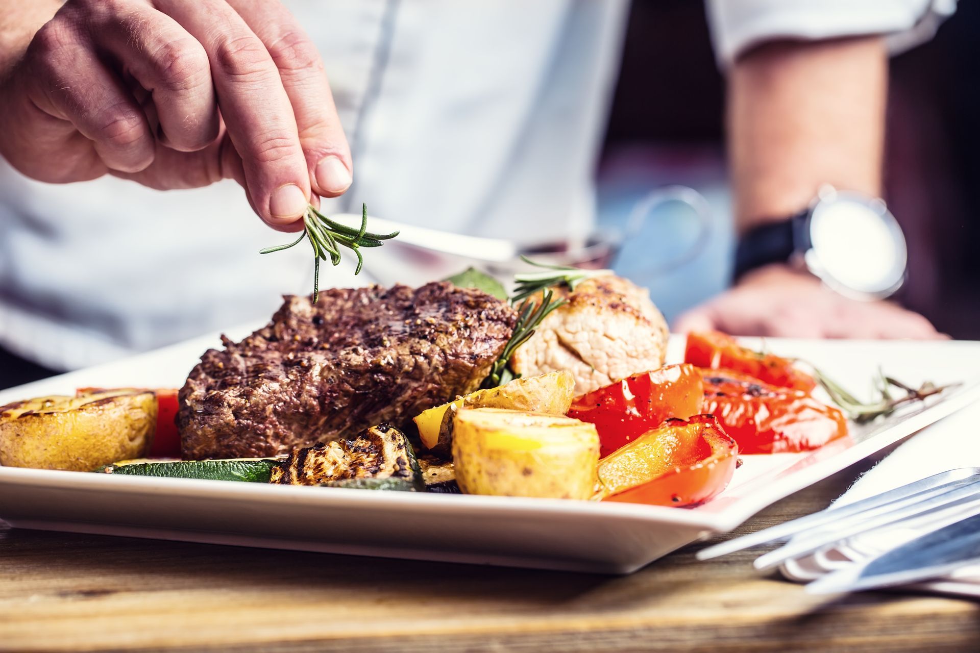 Une personne qui dresse une assiette avec la viande grillée et les légumes.