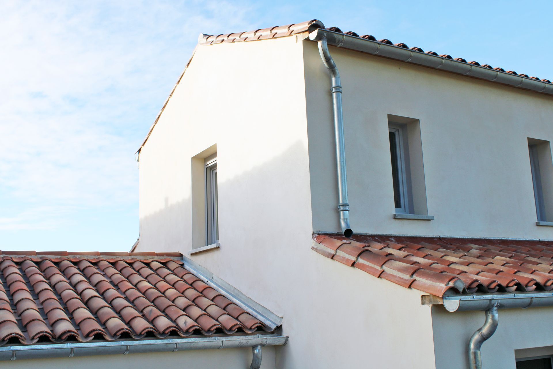 Maison en stuc blanc avec un toit de tuiles rouges et des fenêtres étroites sous un ciel bleu.