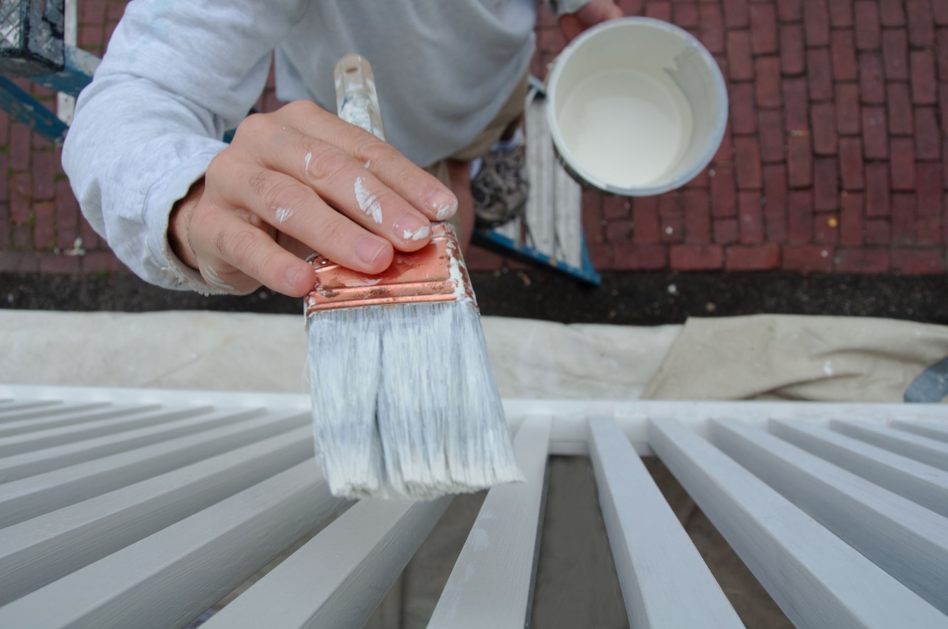 Peinture à la main de lattes blanches avec un pinceau et un gobelet de peinture en extérieur.