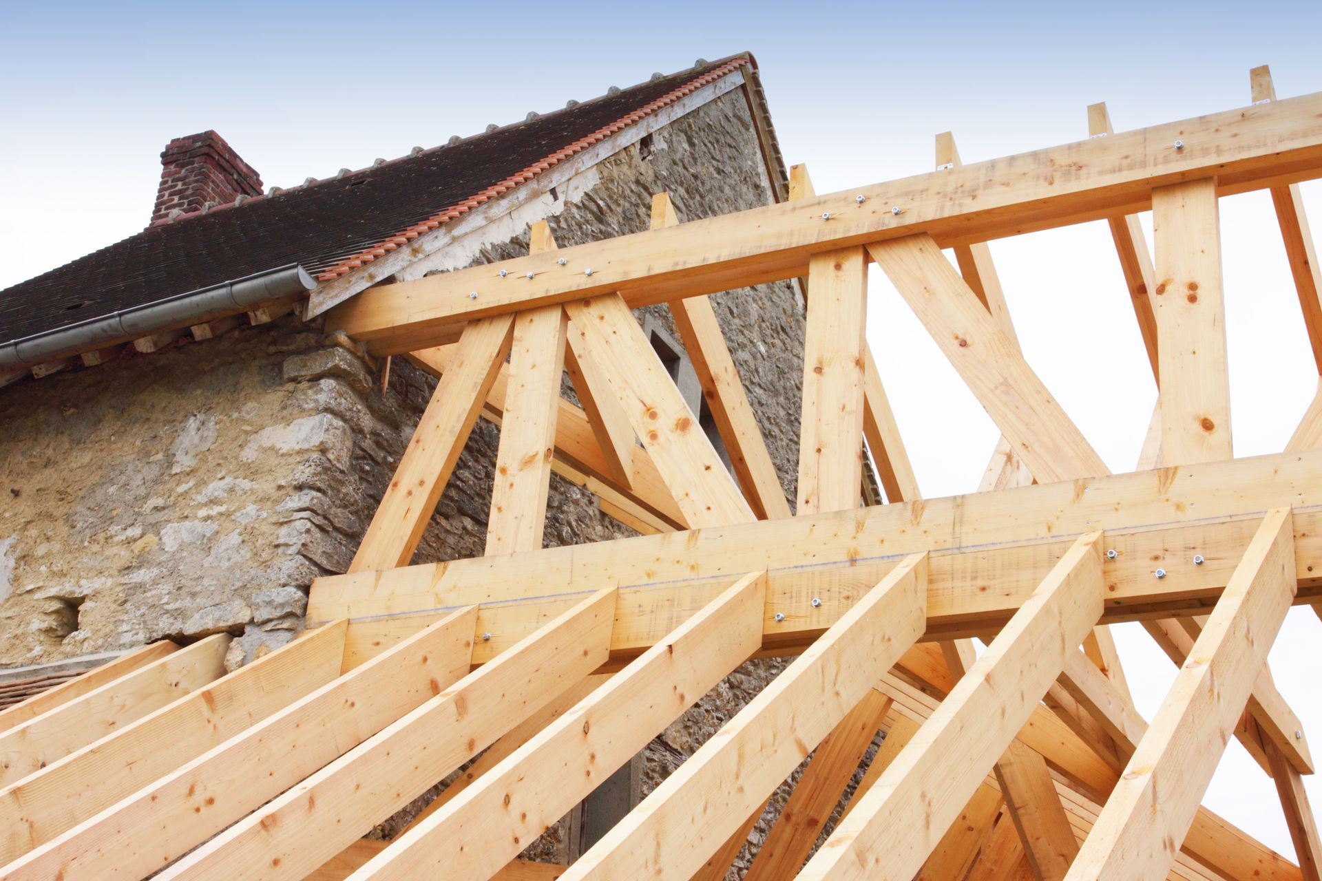 Charpente de toit en bois en construction à côté d'une vieille maison en pierre.