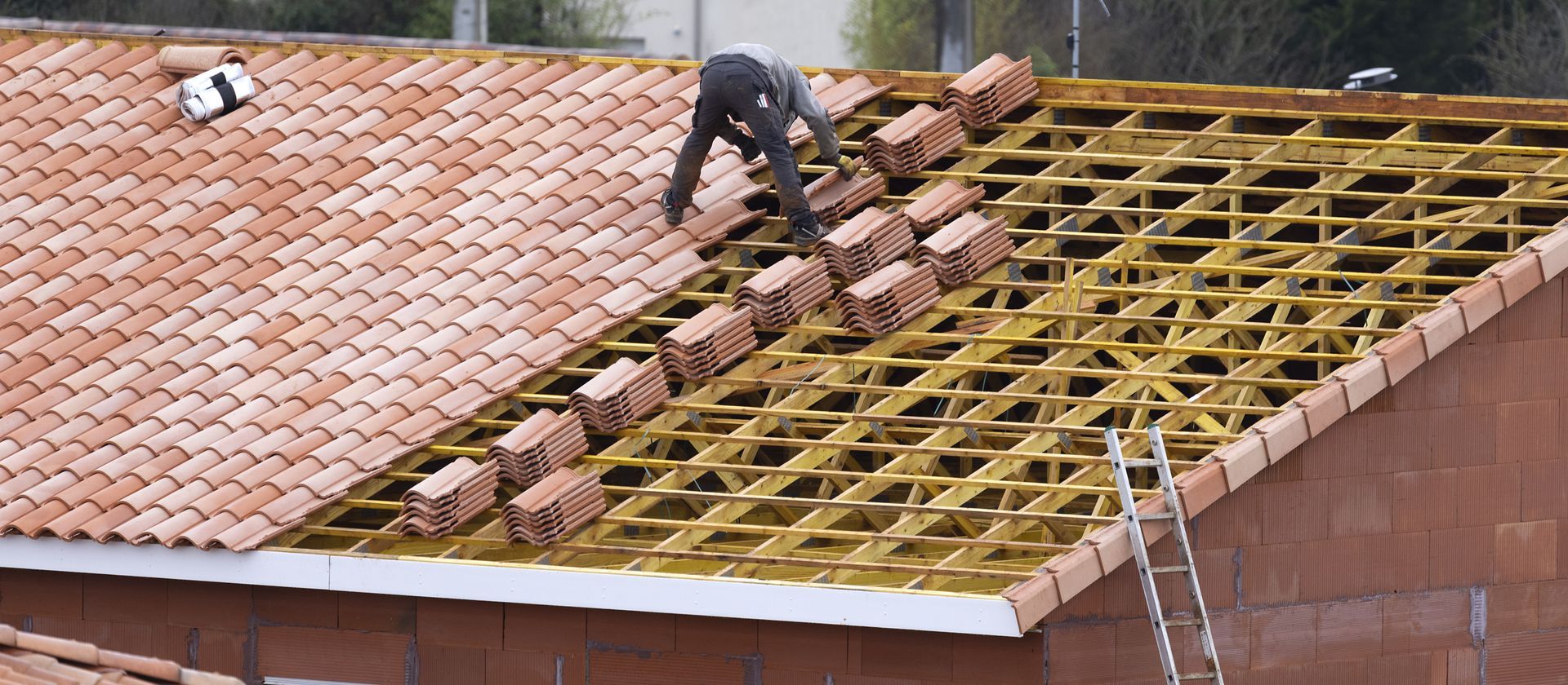 Des ouvriers posent des tuiles sur le toit d'une maison dont la charpente est apparente.