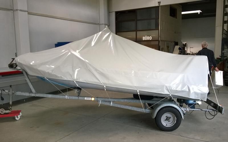 Ein Boot liegt mit einer weißen Plane abgedeckt auf einem Anhänger.