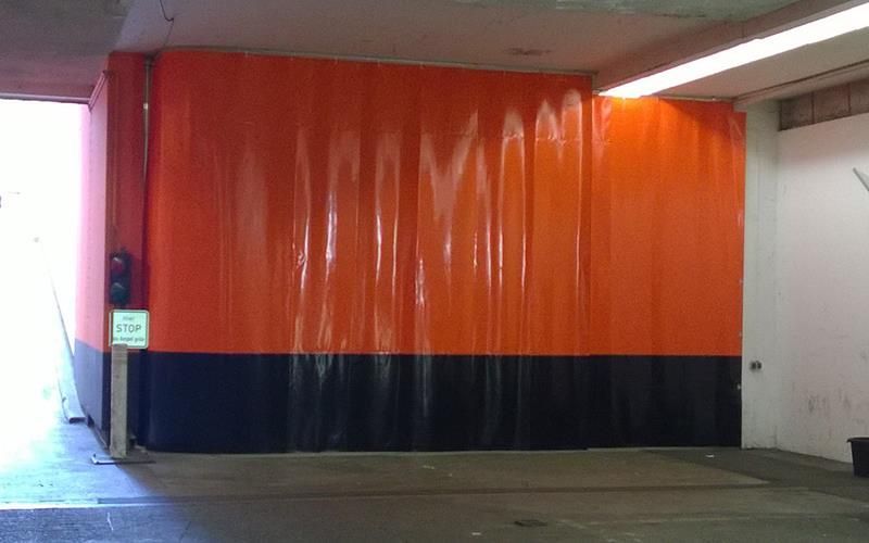 An einer Wand in einer Garage hängt ein orange-schwarzer Vorhang.
