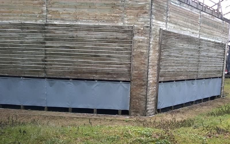 Inmitten einer Wiese steht ein großes Holzgebäude mit einem Metallzaun darum.