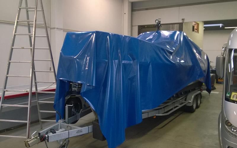 In einer Garage ist ein Boot in eine blaue Plane eingewickelt.