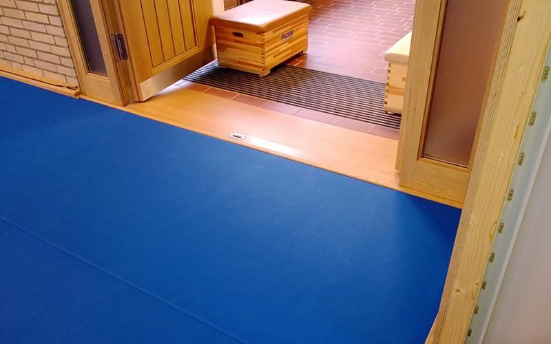In einem Flur liegt neben einer Tür eine blaue Matte auf dem Boden.