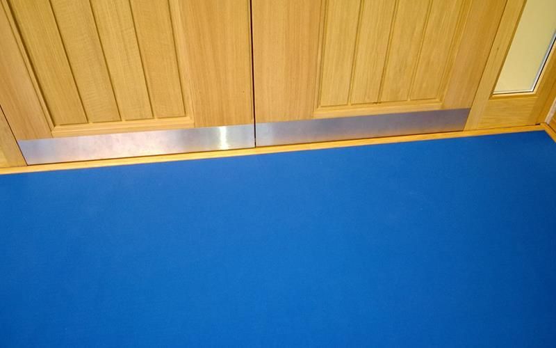 In einem Raum liegt unter einer Holztür eine blaue Matte.
