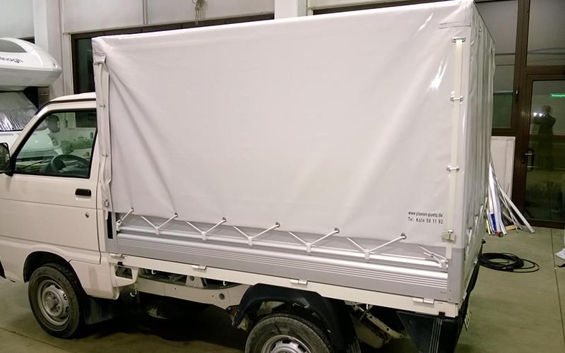 Ein weißer Lastwagen mit weißem Verdeck steht in einer Garage.
