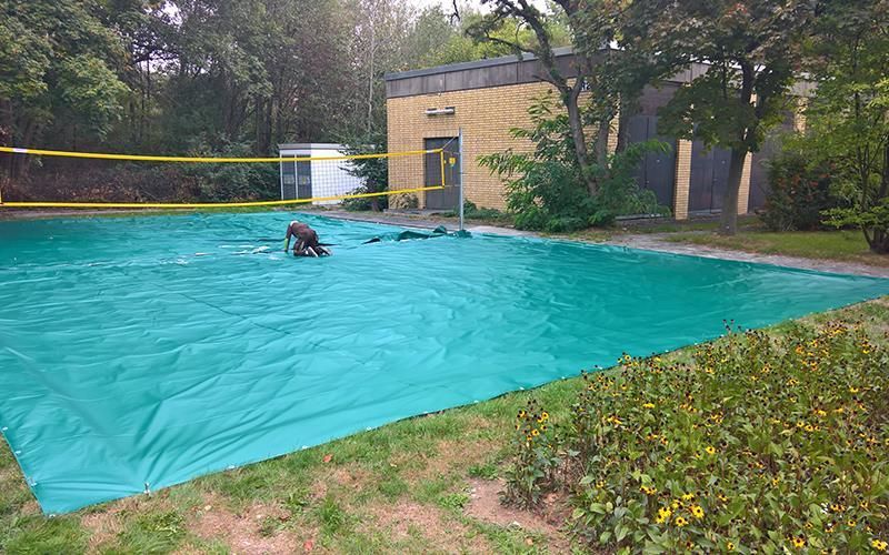 Eine große grüne Plane überdacht ein Volleyballfeld in einem Park.