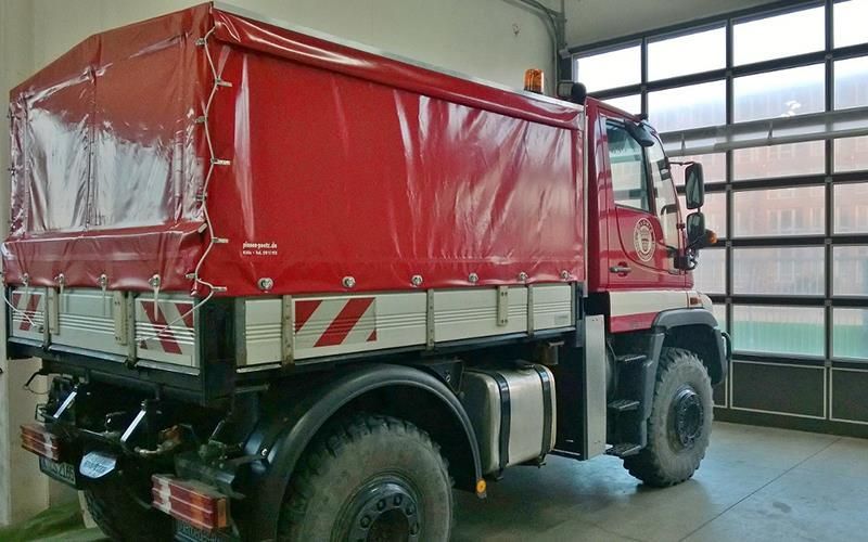 Ein roter Lastwagen mit Plane steht in einer Garage.