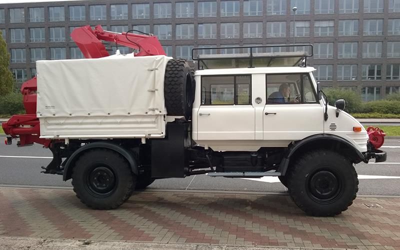 Ein weißer Lastwagen mit einem roten Kran auf der Ladefläche steht am Straßenrand.