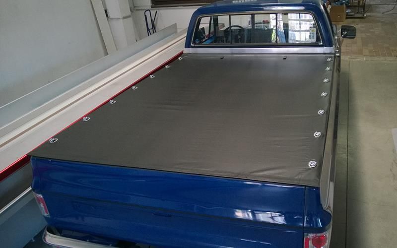In einer Garage steht ein blauer Lastwagen mit einer schwarzen Plane auf der Ladefläche.