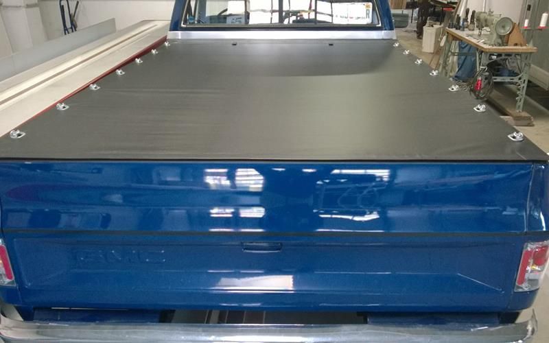 Ein blauer Lastwagen mit einer schwarzen Ladeflächenabdeckung steht in einer Garage.