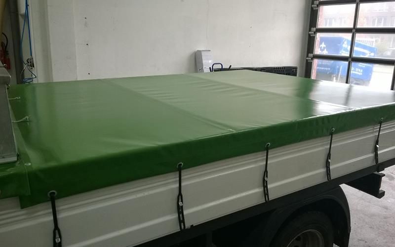 Ein weißer Lastwagen mit einer grünen Plane auf der Ladefläche steht in einer Garage.
