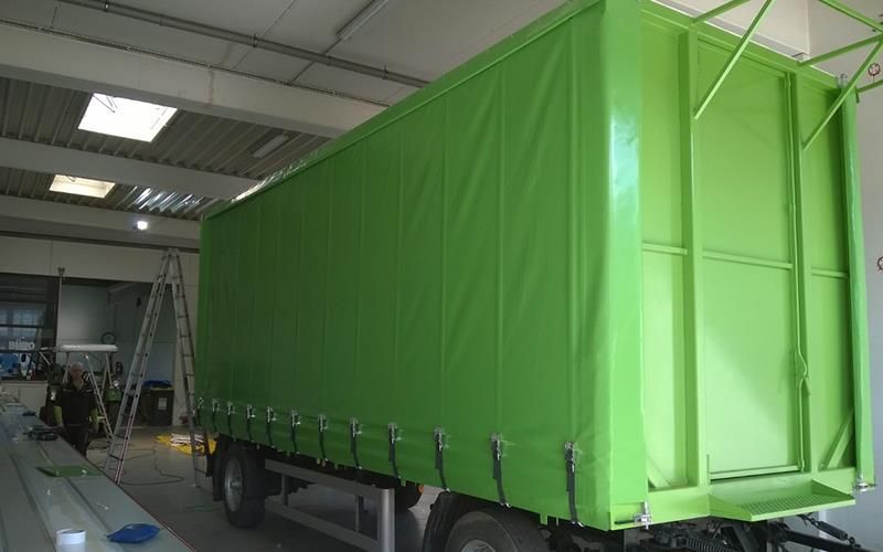 Ein grüner Lastwagen mit einer grünen Plane steht in einer Garage.