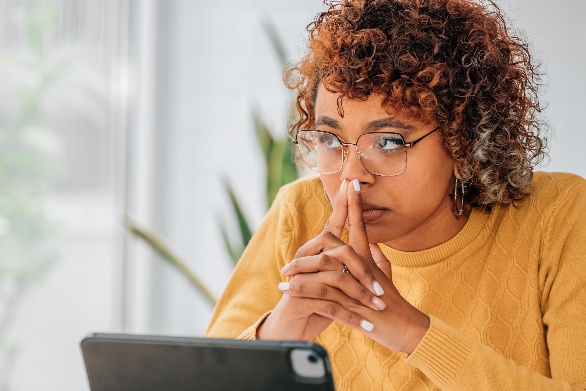 Femme à lunette et pull jaune pensive devant sa tablette