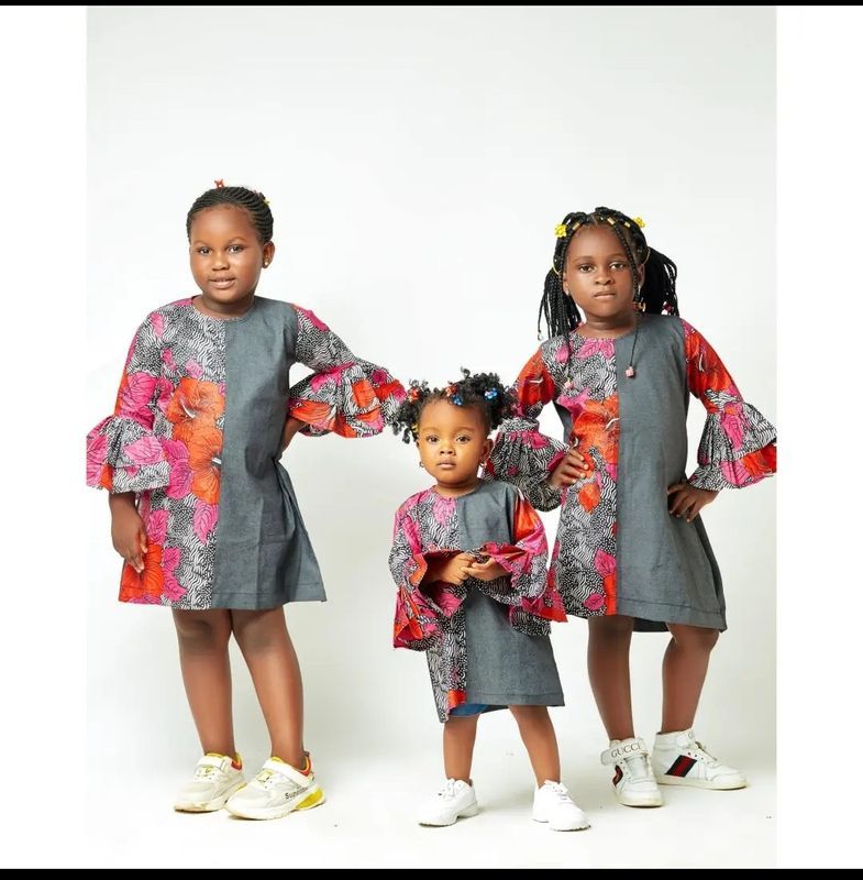 Trois fillettes avec la même robe moitié tissu uni gris et tissu à motif très coloré.