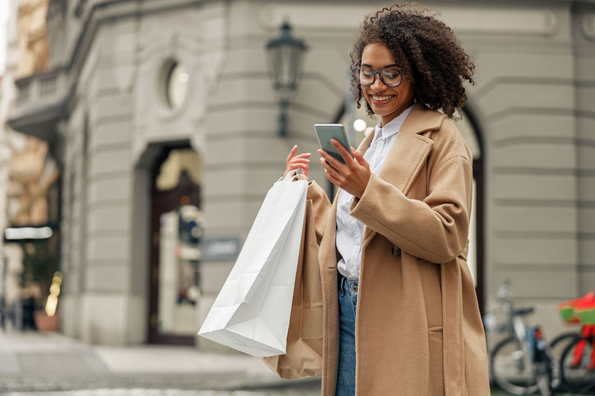 Femme qui regarde son téléphone en tenant des sacs de courses.