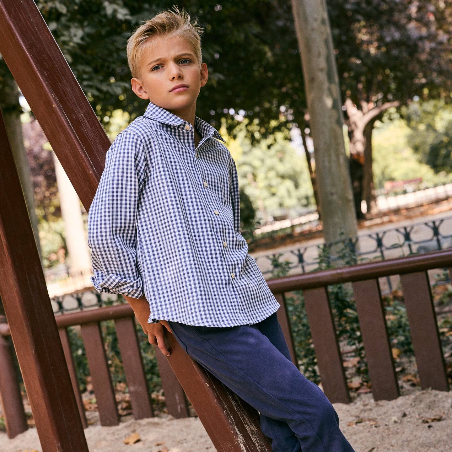 Garçon avec chemise à carreaux bleu et blanche et pantalon marine.