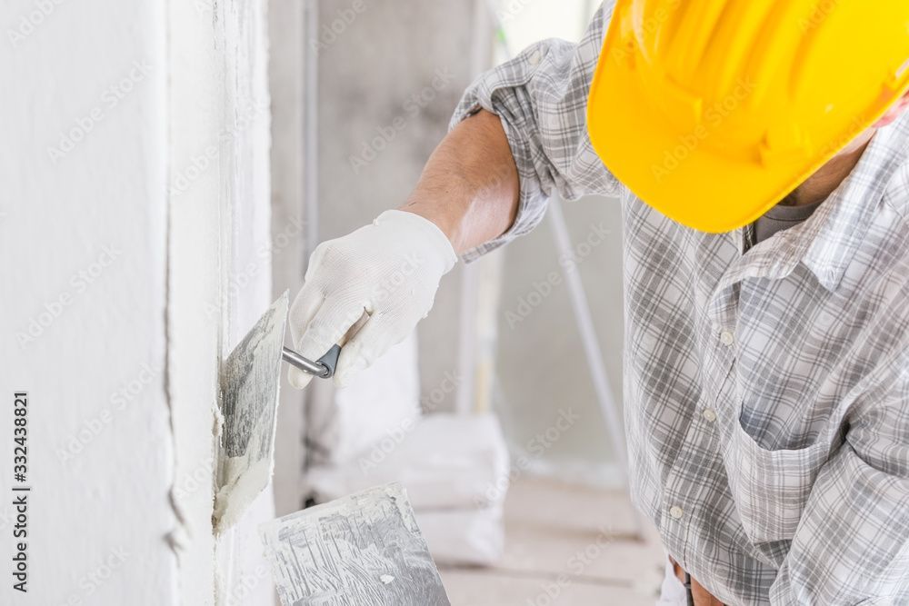 Ein Bauarbeiter streicht mit einem Pinsel eine weisse Wand. Er trägt einen gelben Schutzhelm und Handschuhe.