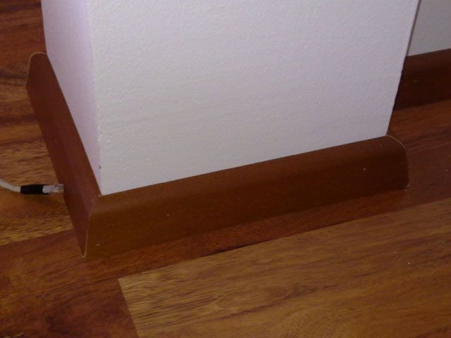 Eine Ecke eines Holzbodens mit einer weißen Zierleiste