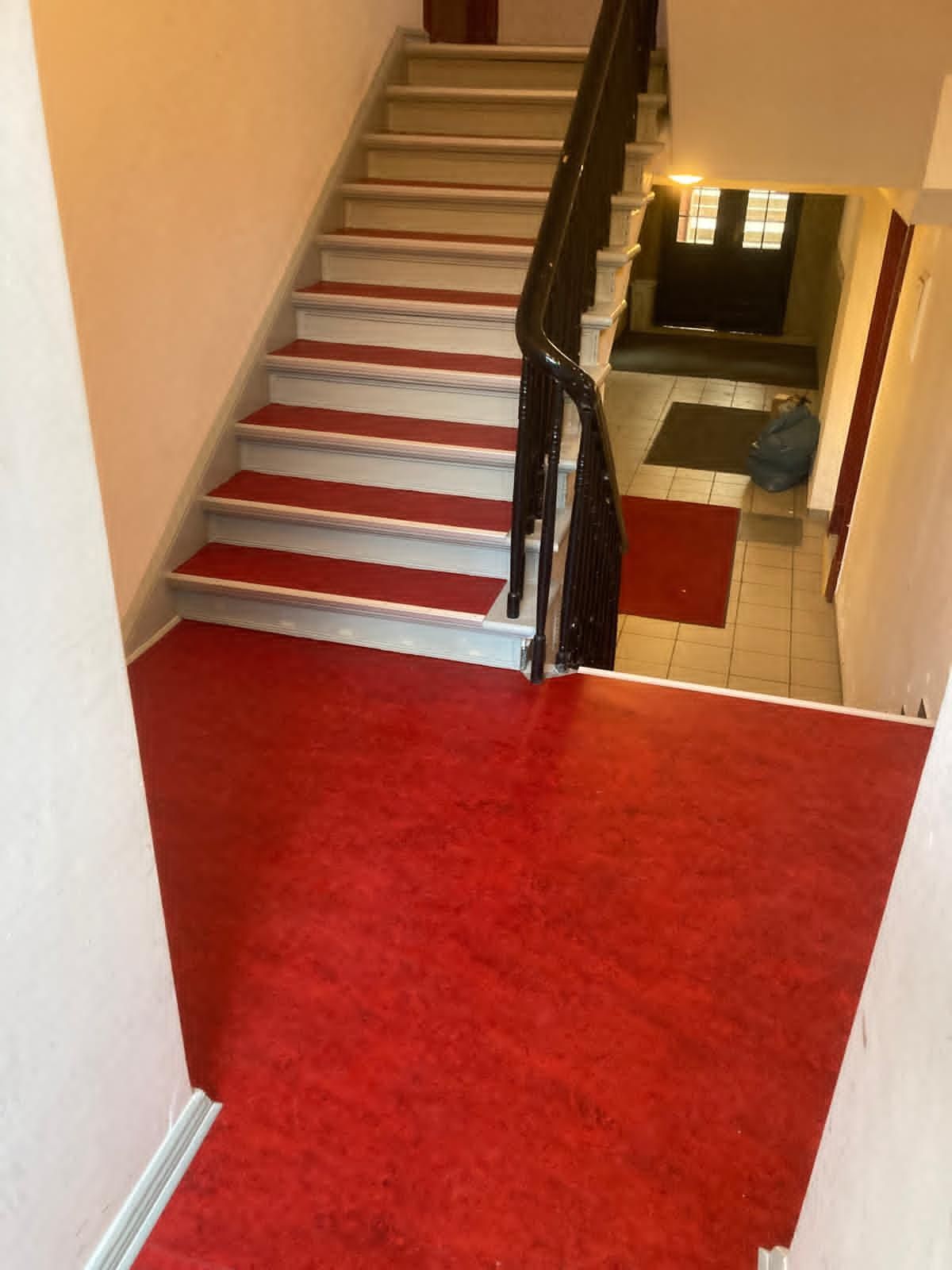 Treppenhaus mit rotem Linoleum und schwarzem Geländer