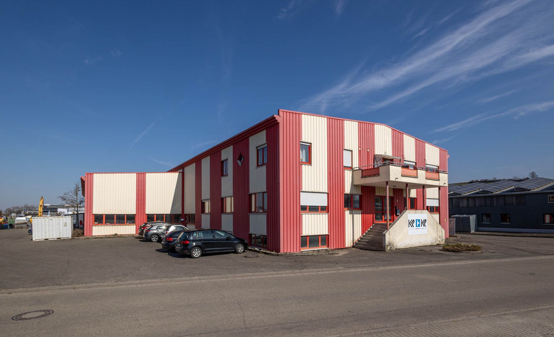 Ein großes rot-weißes Gebäude mit davor geparkten Autos.