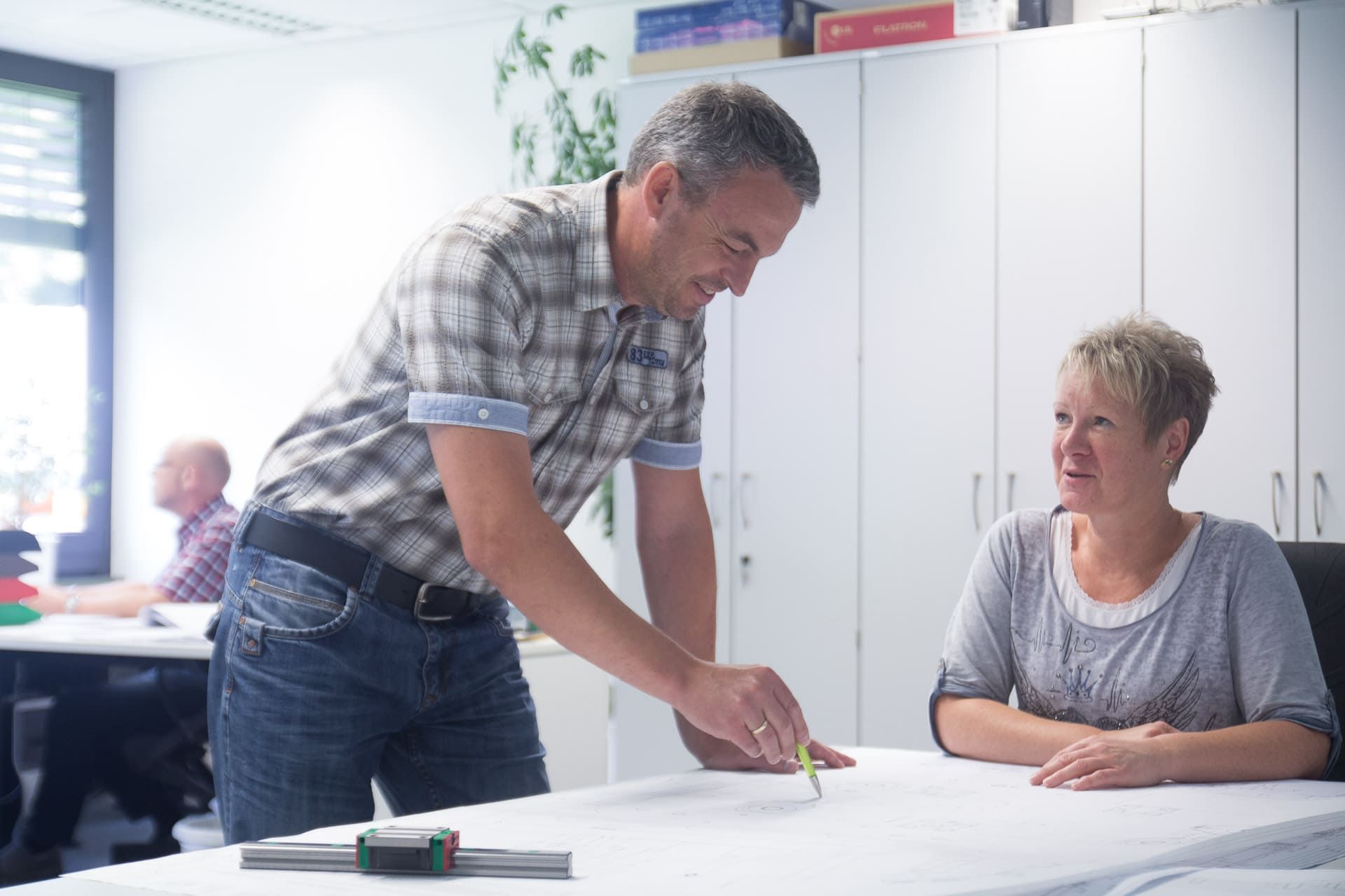 Ein Mann steht neben einer Frau und sitzt an einem Tisch.