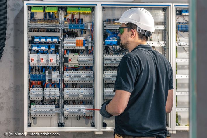 Ein Mann arbeitet mit einem Schraubenzieher an einer Schalttafel.