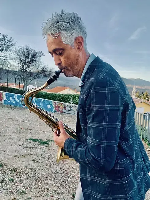 Hombre tocando el saxofón al aire libre cerca de una pared colorida y un cielo nublado.