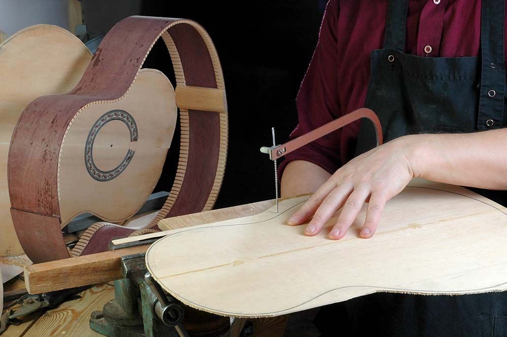 Persona lijando el cuerpo de una guitarra de madera con una lijadora de banda en un taller.