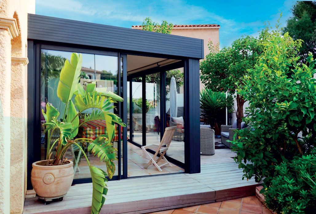 Patio moderne avec portes vitrées, plantes en pot et chaise longue au milieu d'une végétation luxuriante.