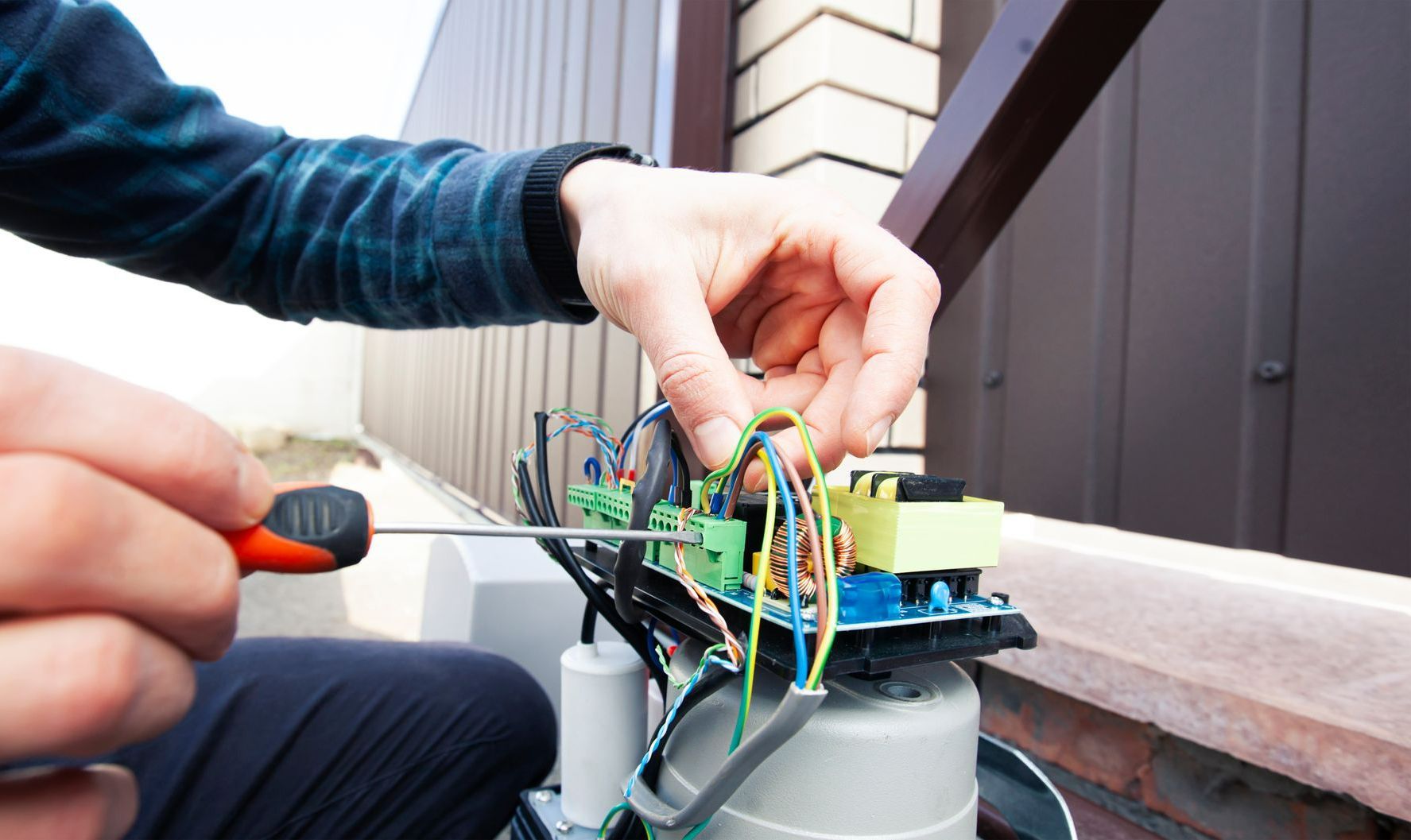 Homme qui fait liaison des câbles sur le moteur d'un portail motorisé.