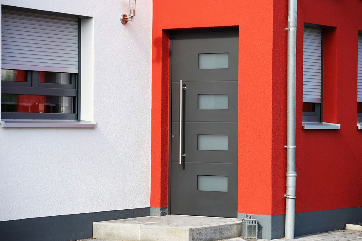 Porte d'entrée en aluminium sur une façade de maison rouge.