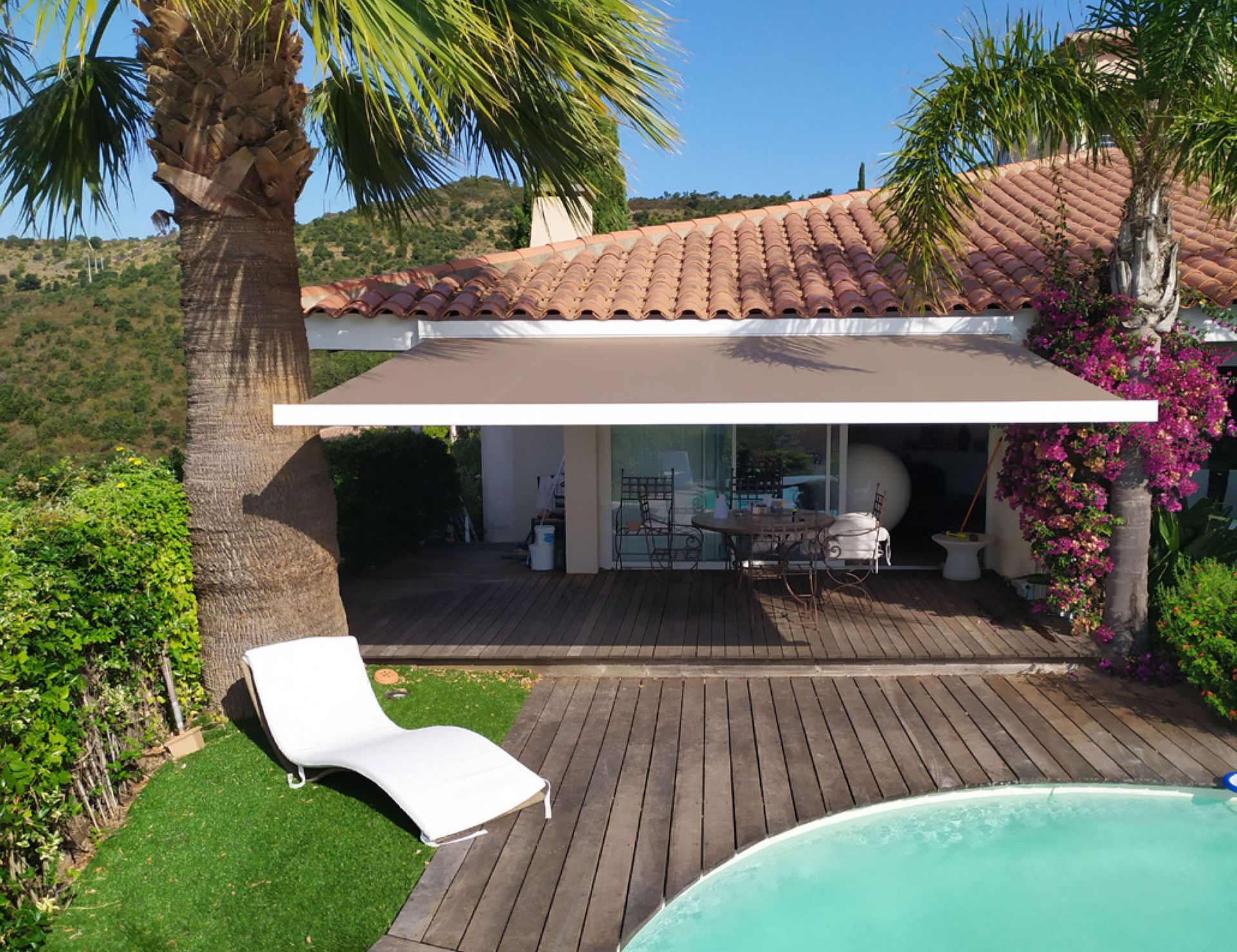 Maison avec terrasse en bois et un grand store banne beige.