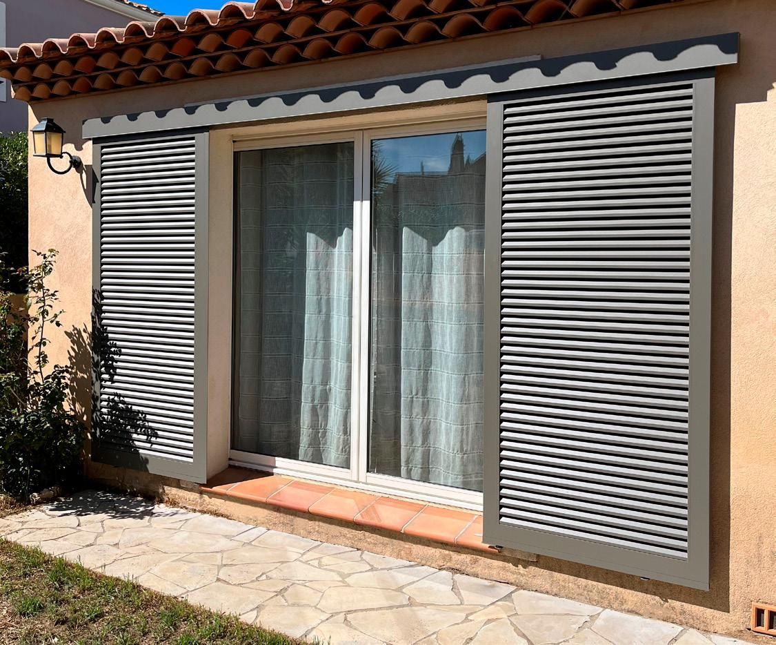Extérieur de la maison avec volets gris fermés encadrant une porte-fenêtre coulissante et une petite terrasse carrelée