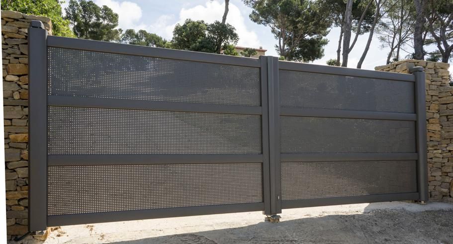 Portail d'allée en métal gris foncé avec panneaux grillagés et piliers en pierre, vu de l'extérieur en plein jour