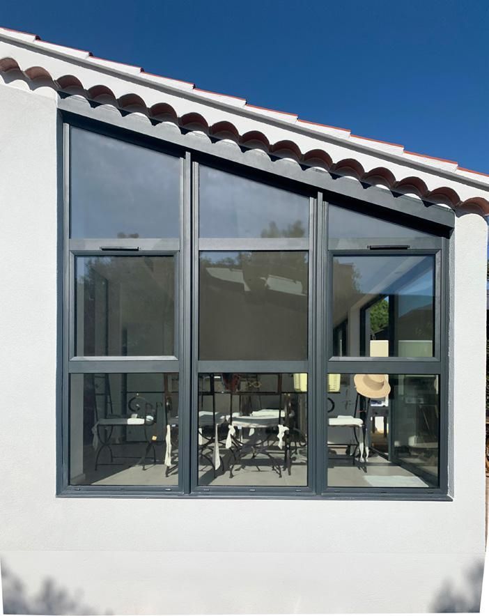 Grande fenêtre sur une maison en stuc blanc, donnant sur une salle à manger moderne à l'intérieur.