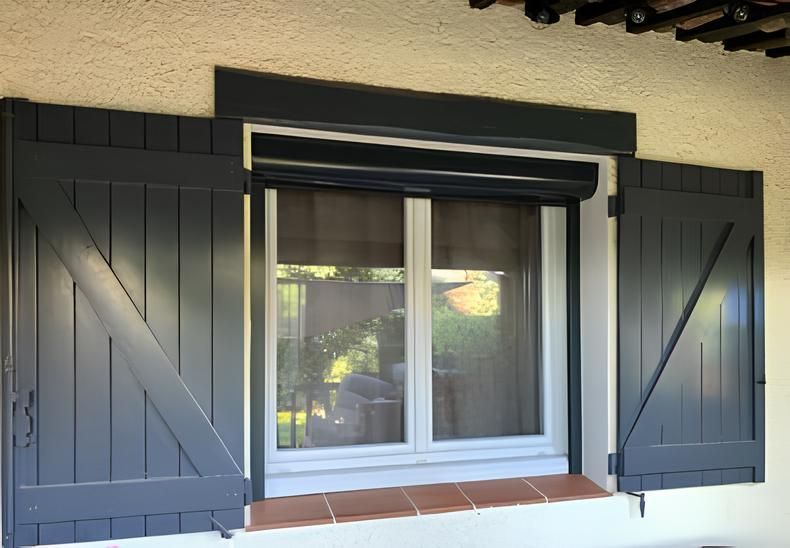 Fenêtre blanche fermée avec volets gris foncé sur un mur extérieur beige