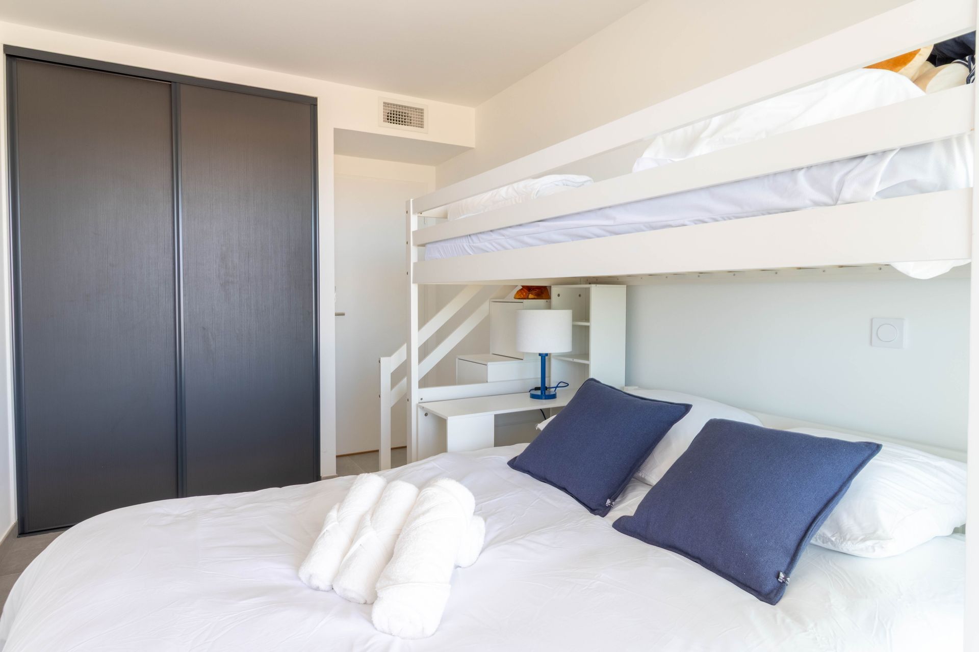 Chambre avec un lit superposé au-dessus d'un lit double, des portes de placard gris foncé et un petit bureau.