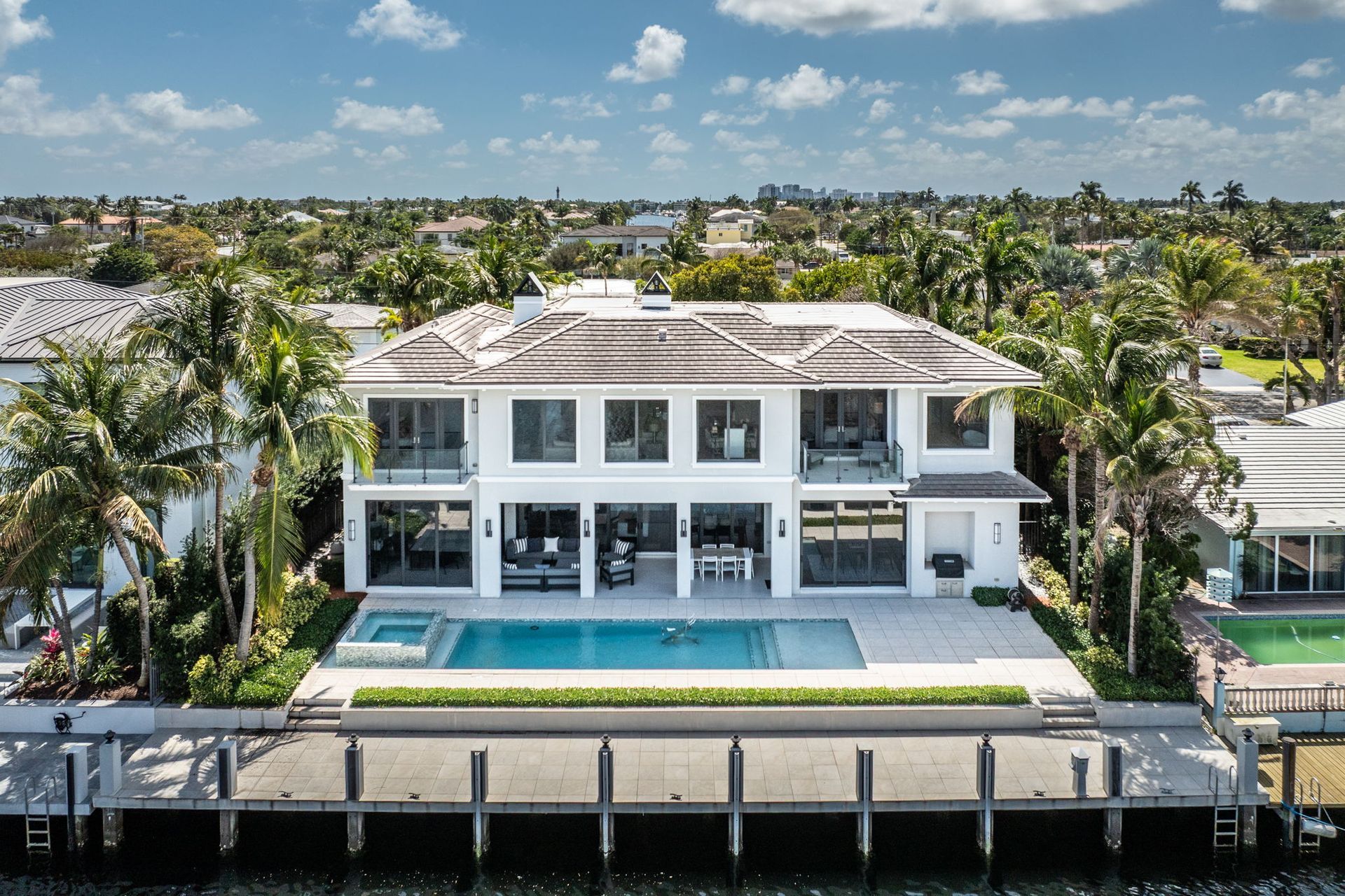Table et chaises de salle à manger sous une canopée de feuillage, avec vue sur une piscine et un vignoble.