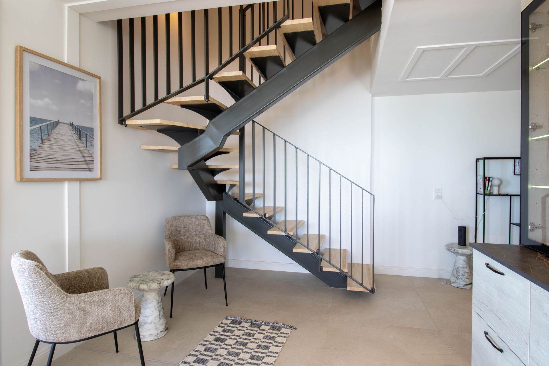 Intérieur moderne avec escalier flottant, deux chaises et œuvres d'art. Murs blancs et marches en bois.