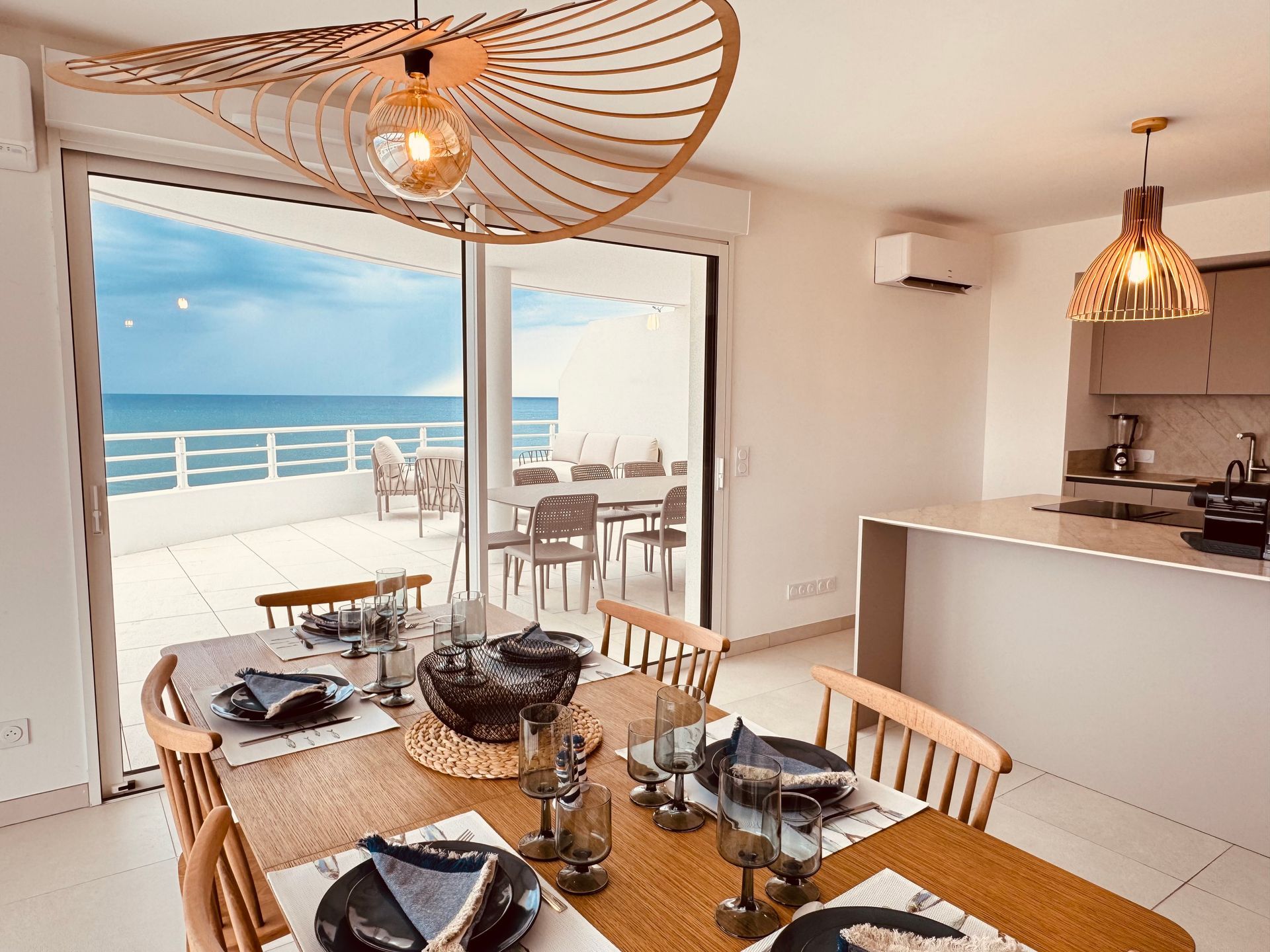 Salle à manger avec vue sur l'océan, table en bois pour six personnes et portes coulissantes ouvertes sur un patio.
