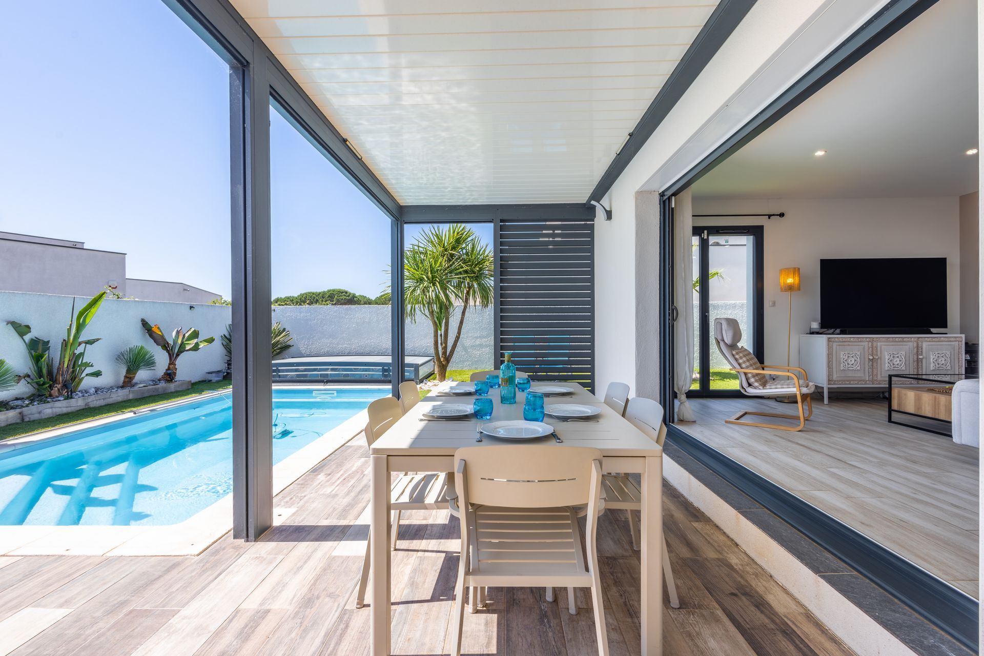 Table et chaises de salle à manger sous une canopée de feuillage, avec vue sur une piscine et un vignoble.