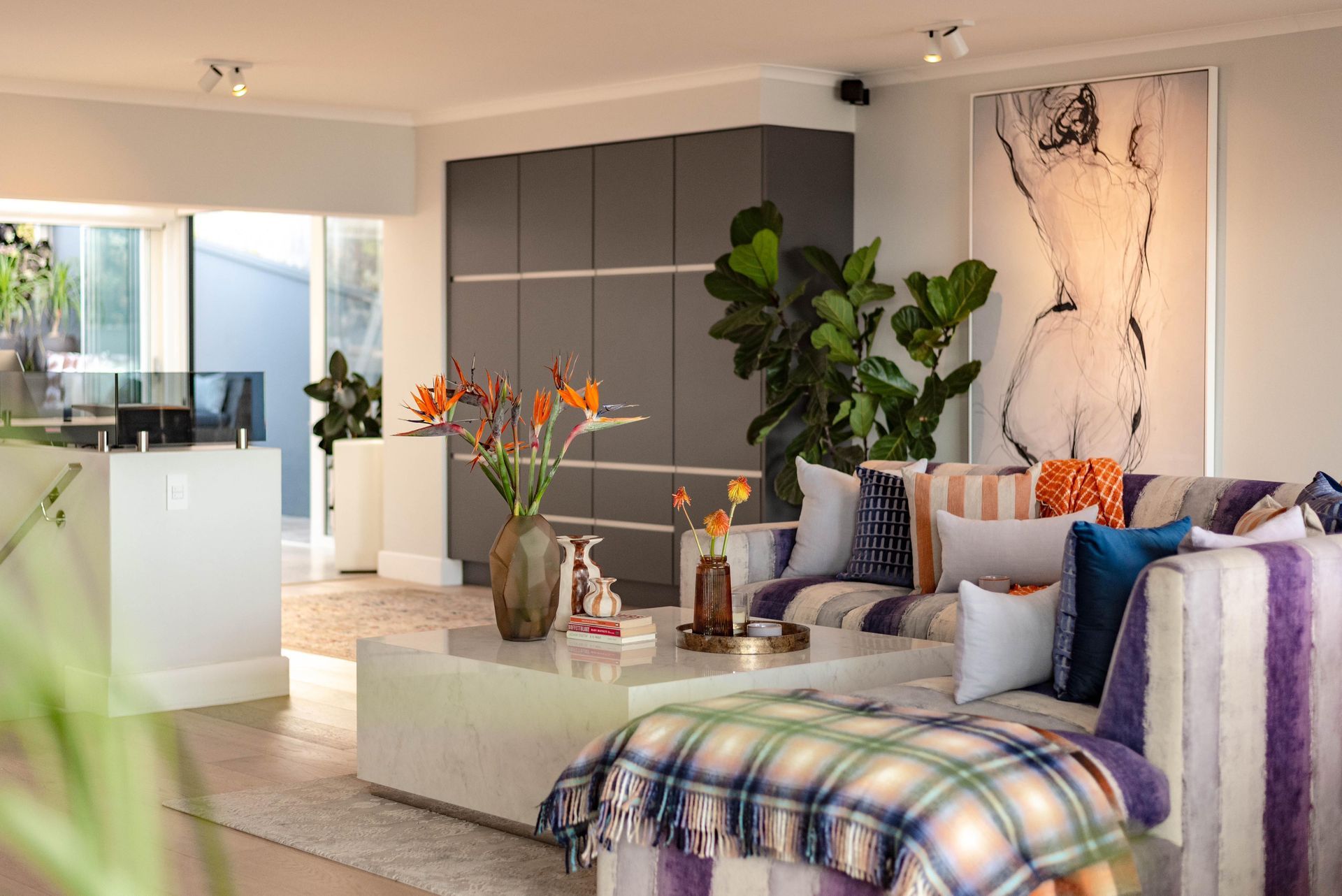 Salon avec meuble de rangement gris, canapé avec coussins colorés et grande œuvre d'art abstraite.